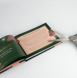Offenes Buch mit Text auf zwei Seiten, dekorative Rahmen und Blumenmuster. Ein Paar Schere liegt auf dem Buch.