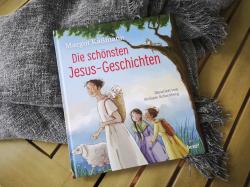 Buchcover mit dem Titel 'Die schönsten Jesus-Geschichten'. Illustration zeigt eine Person mit einem Schaf und zwei Kindern.