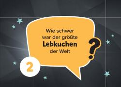 Frage in einem gelben Sprechblasen-Design: Wie schwer war der groesste Lebkuchen der Welt, schwarzer Text auf gelbem Hintergrund, dunkler Hintergrund mit kleinen blauen Sternen.