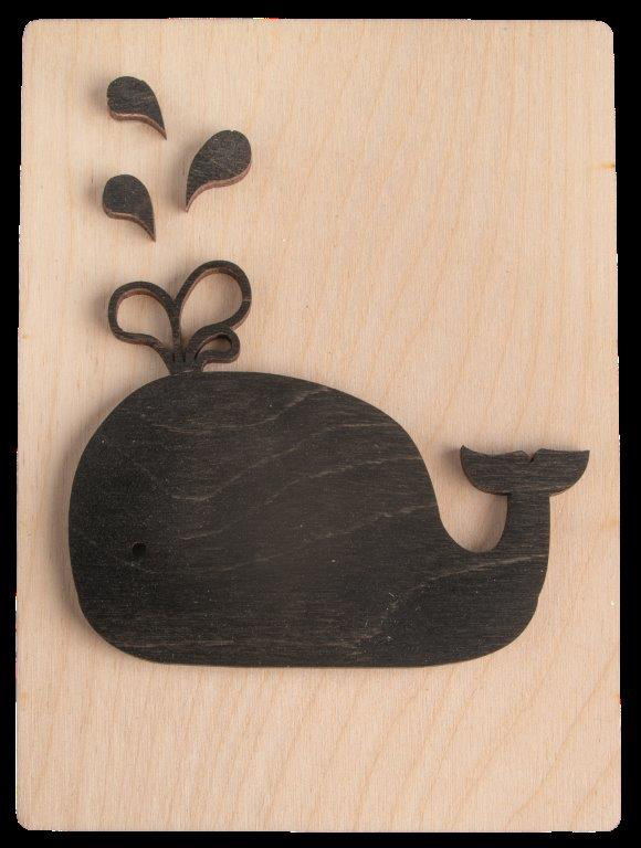 Schwarze Holzfigur eines Wals mit Wasserfontänen. Auf hellem Holzuntergrund.