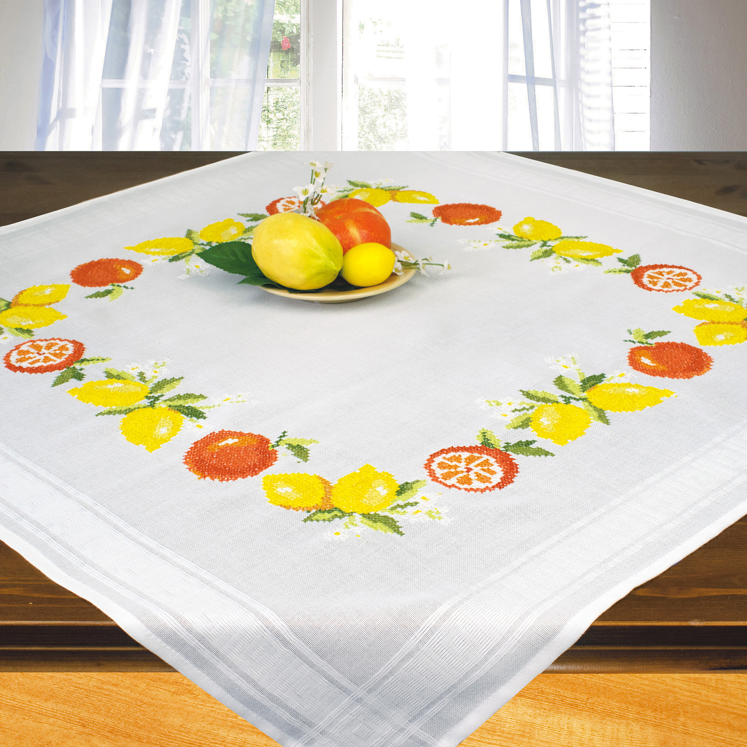 Tischdecke mit buntem Obstmuster. Auf dem Tisch liegt eine Schale mit verschiedenen Früchten.