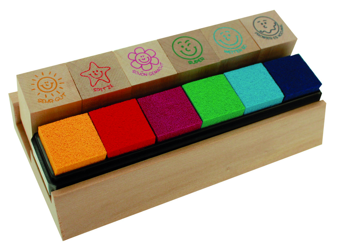 Holzblock mit sechs bunten Schwämmchen. Farben: orange, rot, lila, grün, blau. Oben fünf Stempel mit Smiley-Gesichtern und positiven Worten.