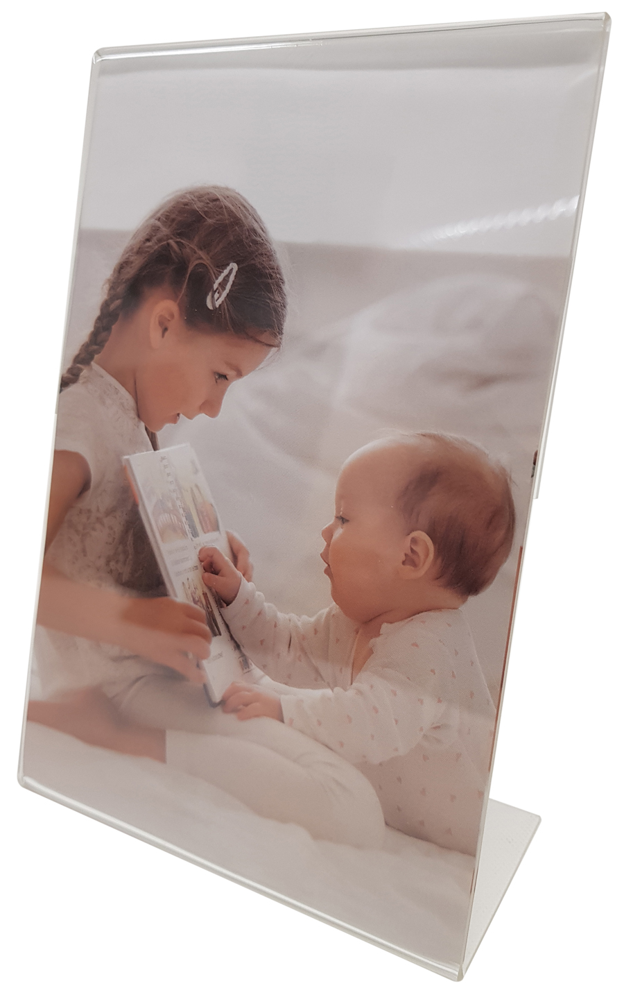 Ein Mädchen mit geflochtenem Haar sitzt auf einem Bett und zeigt einem Baby ein Bilderbuch. Beide schauen konzentriert auf das Buch. Das Mädchen trägt ein helles Oberteil, das Baby einen weißen Schlafanzug.