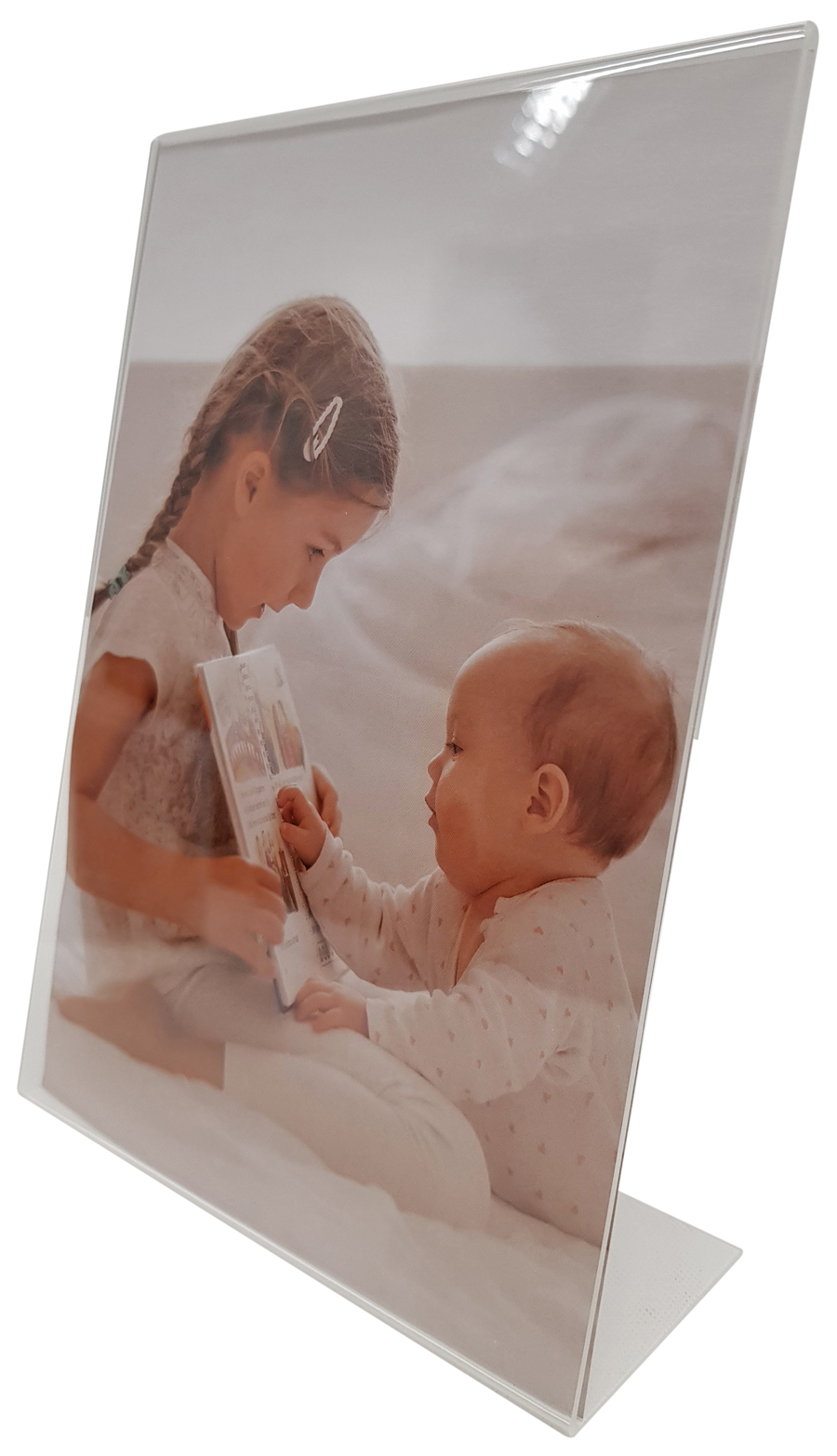 Ein Mädchen liest einem Baby ein Buch vor. Beide sitzen auf einem Bett mit weißen Laken.