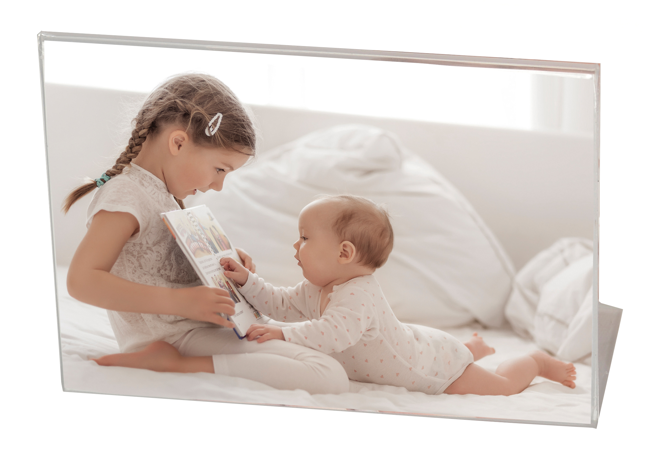 Ein Mädchen liest einem Baby ein Buch vor. Beide sitzen auf einem Bett mit weißen Laken.